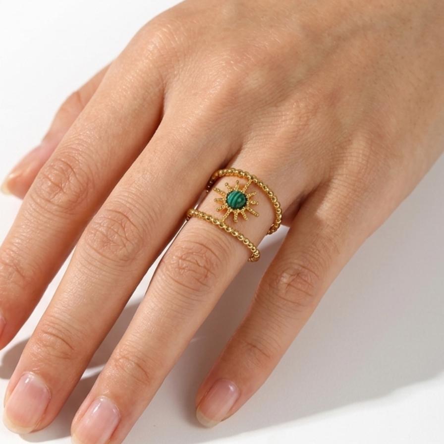 Hand wearing a gold ring with a green gemstone on a white background