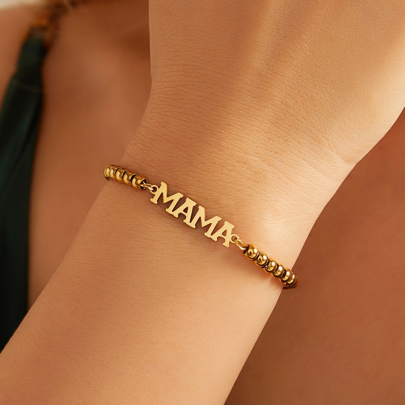 Gold 'MAMA' bracelet on a person's wrist with a blurred background