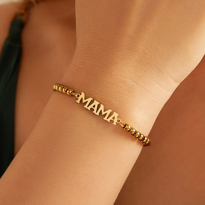 Gold 'MAMA' bracelet on a person's wrist with a blurred background