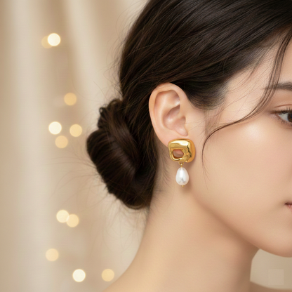 Gold earring with a pearl drop worn by a model against a soft, blurred background