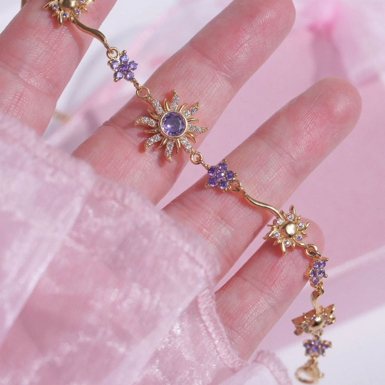 Delicate gold ring with purple gemstones on a pink fabric background