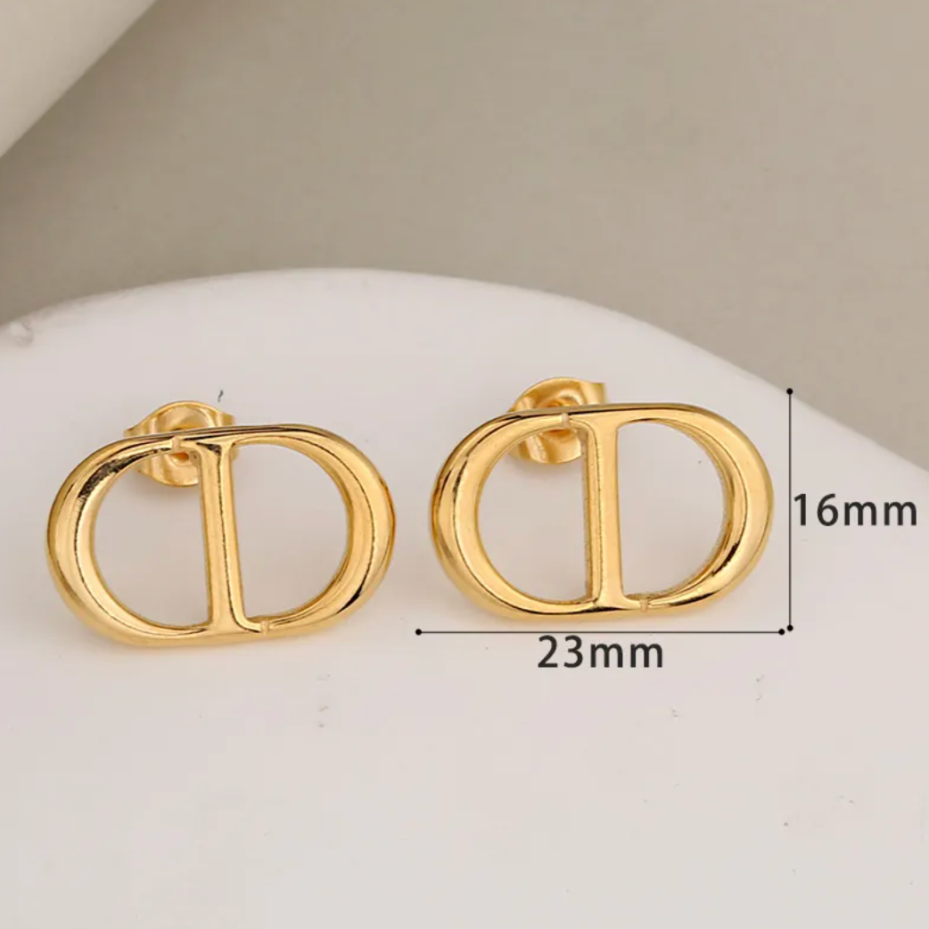 A pair of gold-toned double-D logo stud earrings displayed on a white curved surface, with measurement annotations showing 16mm height and 23mm width.