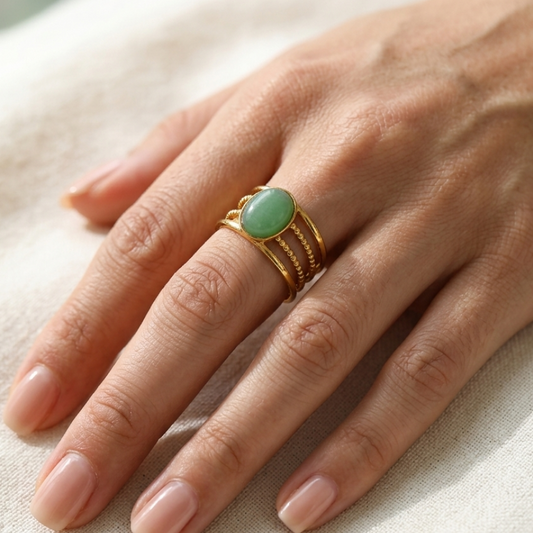 Hand wearing a gold ring with a green stone on a light background