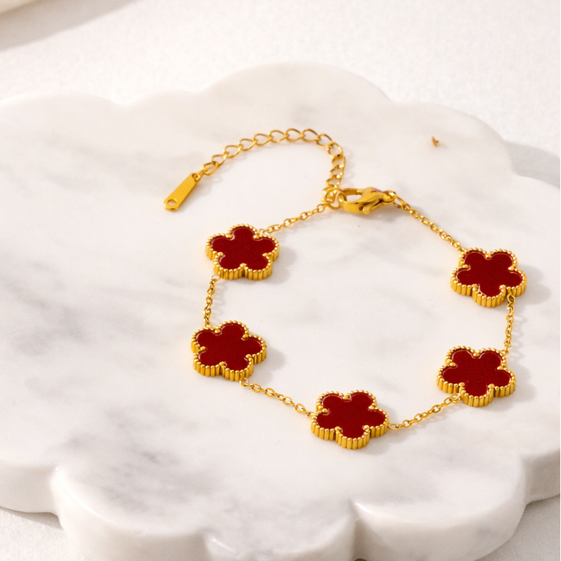 Gold bracelet with red flower-shaped charms on a white shell