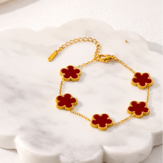 Gold bracelet with red flower-shaped charms on a white shell
