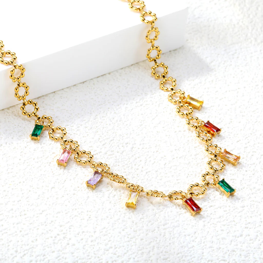 Gold necklace with colorful gemstone pendants on a white surface